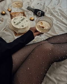 a woman in fishnet stockings holding a wine glass and cake on a white tablecloth