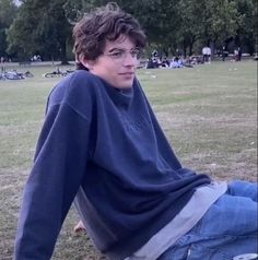 a young man sitting on top of a grass covered field