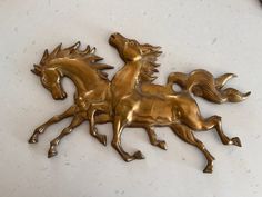 two golden horses that are standing next to each other on a white counter top with a clock in the background