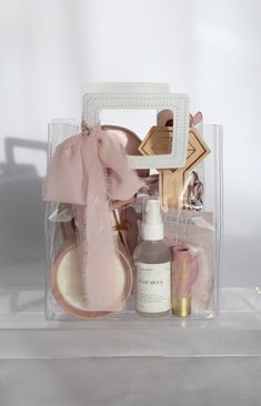 the contents of a beauty kit in a clear plastic bag on a white surface with a pink ribbon