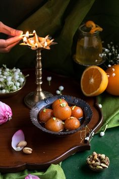 there is a bowl full of oranges on the table with flowers and nuts around it