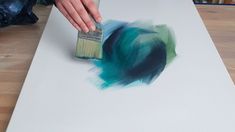 a person is using a brush to paint a piece of paper with blue and green colors