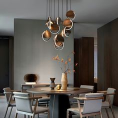 a dining room table with chairs and vases on it in front of a gray wall