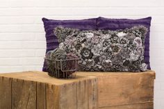 a purple pillow with flowers on it sitting on a wooden bench