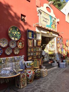 an outdoor market with many plates and bowls on the outside, along side a red building