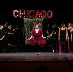 a woman in a red dress is dancing on stage with other people and musicians behind her