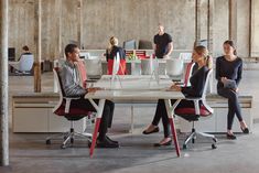 four people sitting at a table in an office setting with chairs and desks around them