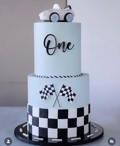 a three tiered cake with cars on top is decorated in white and black checkered