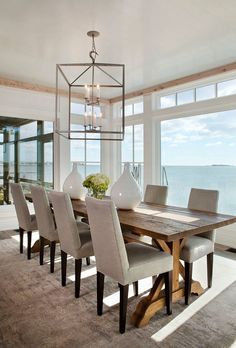 a dining room table with chairs and a vase on top of it in front of a large window overlooking the ocean