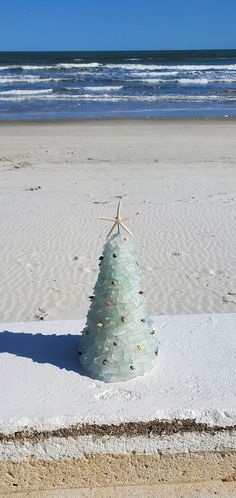 a glass christmas tree sitting on top of a white sandy beach next to the ocean