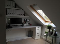 a desk with a computer on top of it under a slanted skylight in a room