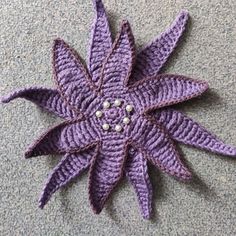 a crocheted purple flower with pearls on it's center sits on the floor