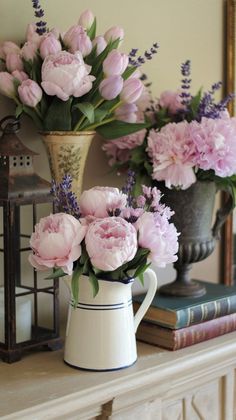 some pink flowers are sitting in a vase on a mantle next to an old book