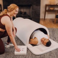 a woman is looking at a man laying on the floor next to a large white object