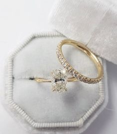 an engagement ring is sitting on top of a white cloth box with the wedding band in gold