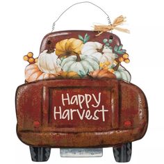 a happy harvest sign hanging from the side of a red truck with pumpkins and gourds in it