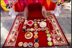 a red table topped with lots of different types of food on top of a rug