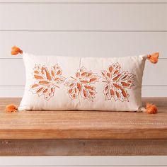 an orange embroidered pillow with tassels sits on a wooden table