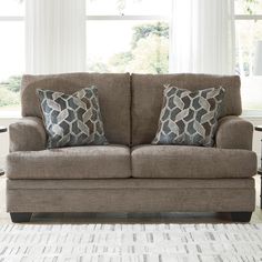 a couch with two pillows on top of it in front of a rug and windows