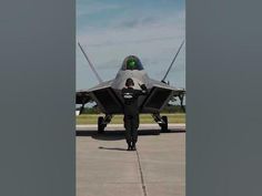 a fighter jet sitting on top of an airport tarmac next to a man standing in front of it