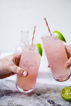 two people holding glasses with drinks and limes