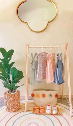 there is a potted plant next to a rack with clothes on it and two baby shoes in the foreground