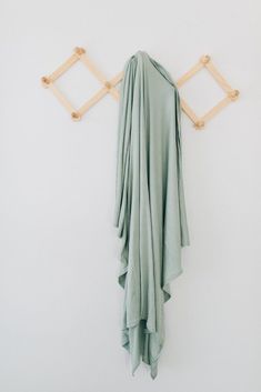 a green dress hanging on a white wall with wooden pegs and clothes pins attached to it