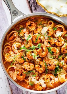 a skillet filled with pasta and shrimp on top of a wooden table next to a spoon