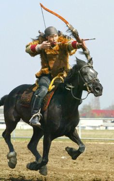 a man riding on the back of a black horse while holding a bow and arrow