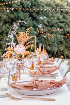 an outdoor table set with place settings and flowers