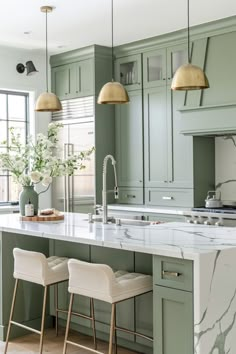 a kitchen with green cabinets and marble counter tops, gold pendant lights over the island