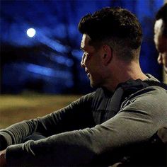 two men sitting next to each other in front of a building at night with the lights on