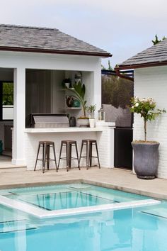 an outdoor kitchen next to a pool with bar stools