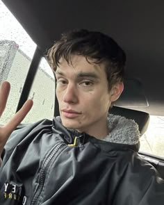 a man sitting in the back seat of a car with his hand up to the camera