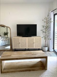 a flat screen tv sitting on top of a wooden table in a living room next to a window