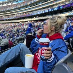 a woman sitting in the stands at a football game eating and drinking from a cup