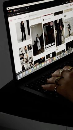 a person's hand is on the keyboard of a laptop computer, which displays images of women in black outfits