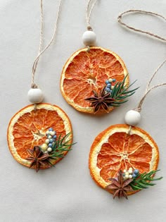 three orange slices are hanging from twine strings on a white tablecloth, decorated with christmas decorations