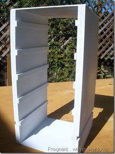 an open white refrigerator sitting on top of a wooden table next to a fence and trees