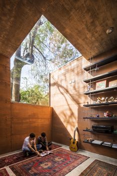 two people sitting on the floor in front of a wooden wall with shelves and rugs