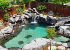 an outdoor pool with waterfall and rocks in the water, surrounded by trees and bushes