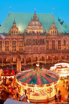 an outdoor christmas market in front of a large building with lots of lights on it