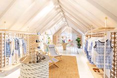 the inside of a clothing store with clothes on racks and chairs in front of them