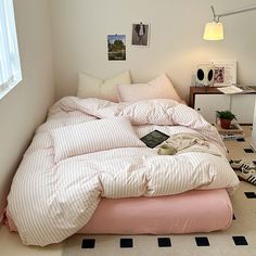 an unmade bed with pink and white comforter in a bedroom next to a window