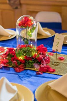 the table is set with plates, napkins and flowers in a glass dome on top