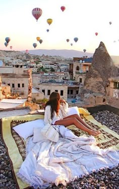 a woman sitting on top of a bed next to hot air balloons in the sky