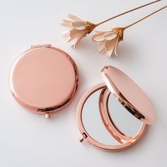 the compact mirror is next to a flower on a white surface with pink petals in it