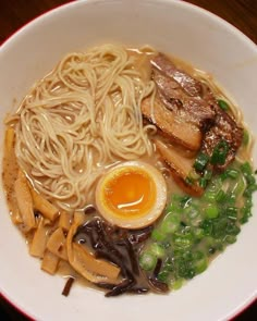 a white bowl filled with noodles, meat and veggies next to an egg