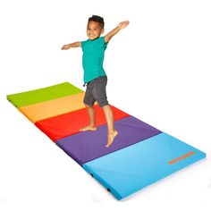 a little boy standing on top of a rainbow colored mat with his arms spread out