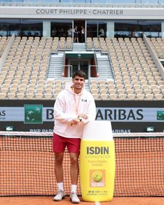 a man standing on a tennis court with a racquet in his hand next to a trash can